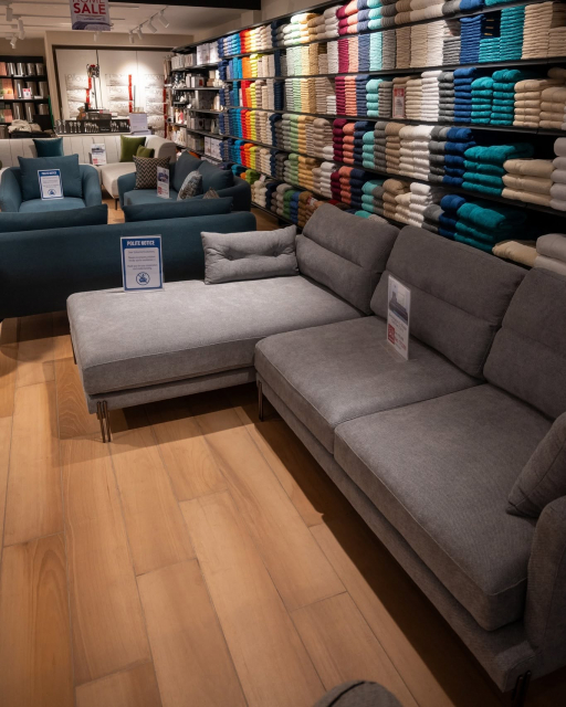 Store interior with sofas in the foreground and shelves of folded towels along the back wall.