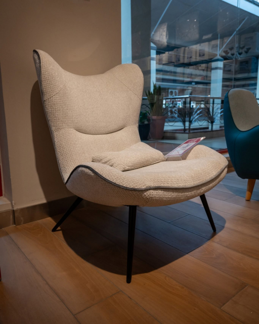 Cream wingback lounge chair with black tapered legs displayed near a shop window.
