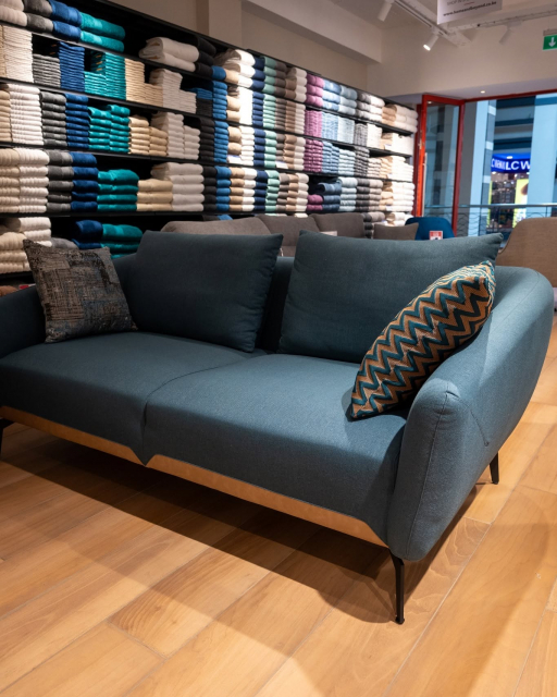 Blue upholstered sofa with patterned cushions displayed in front of neatly stacked towels.