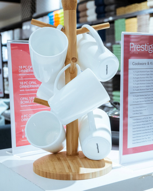 White ceramic mugs hanging from a wooden stand in a cookware and dinnerware display.