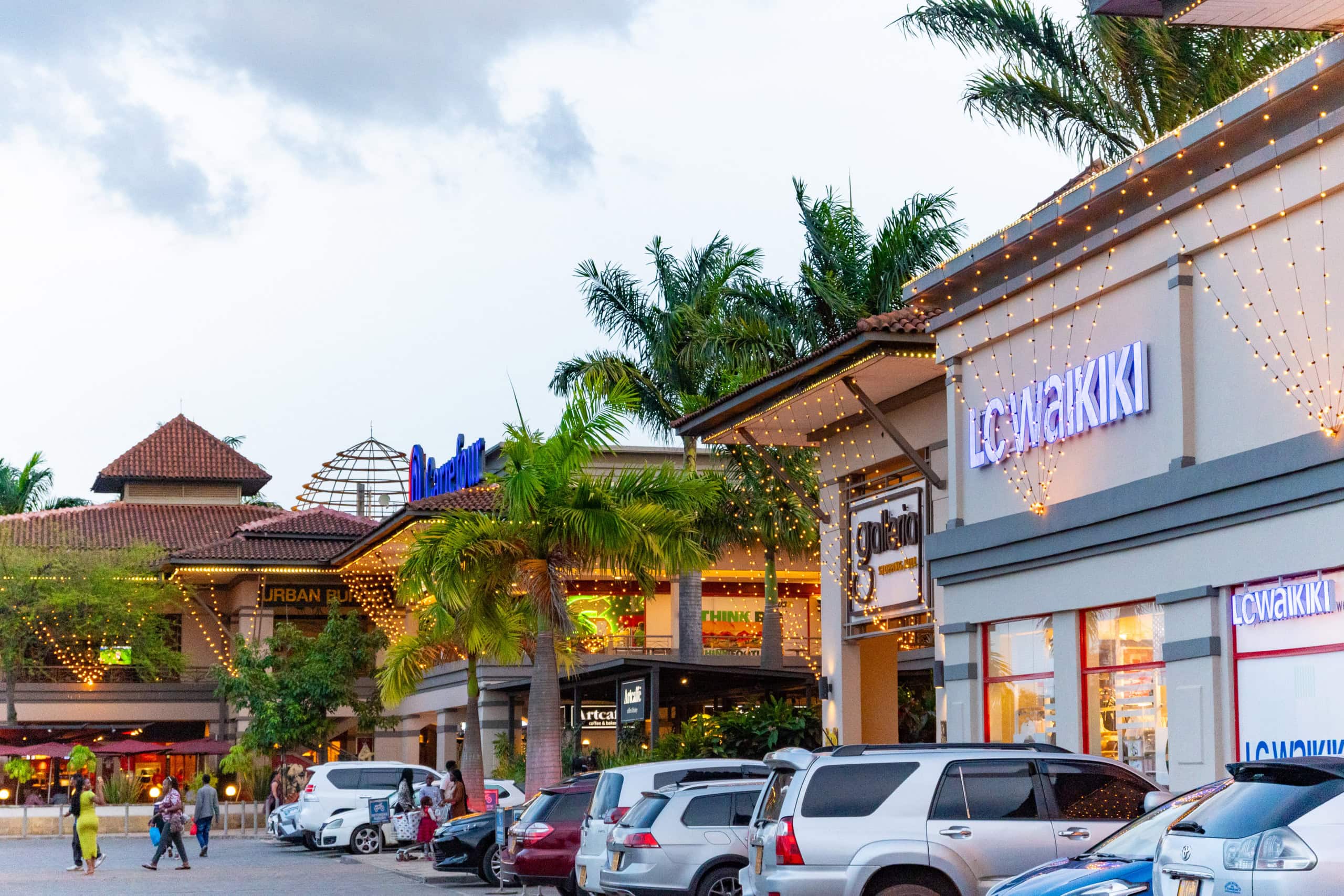 Outdoor shopping complex with palm trees, parked cars, and illuminated storefronts