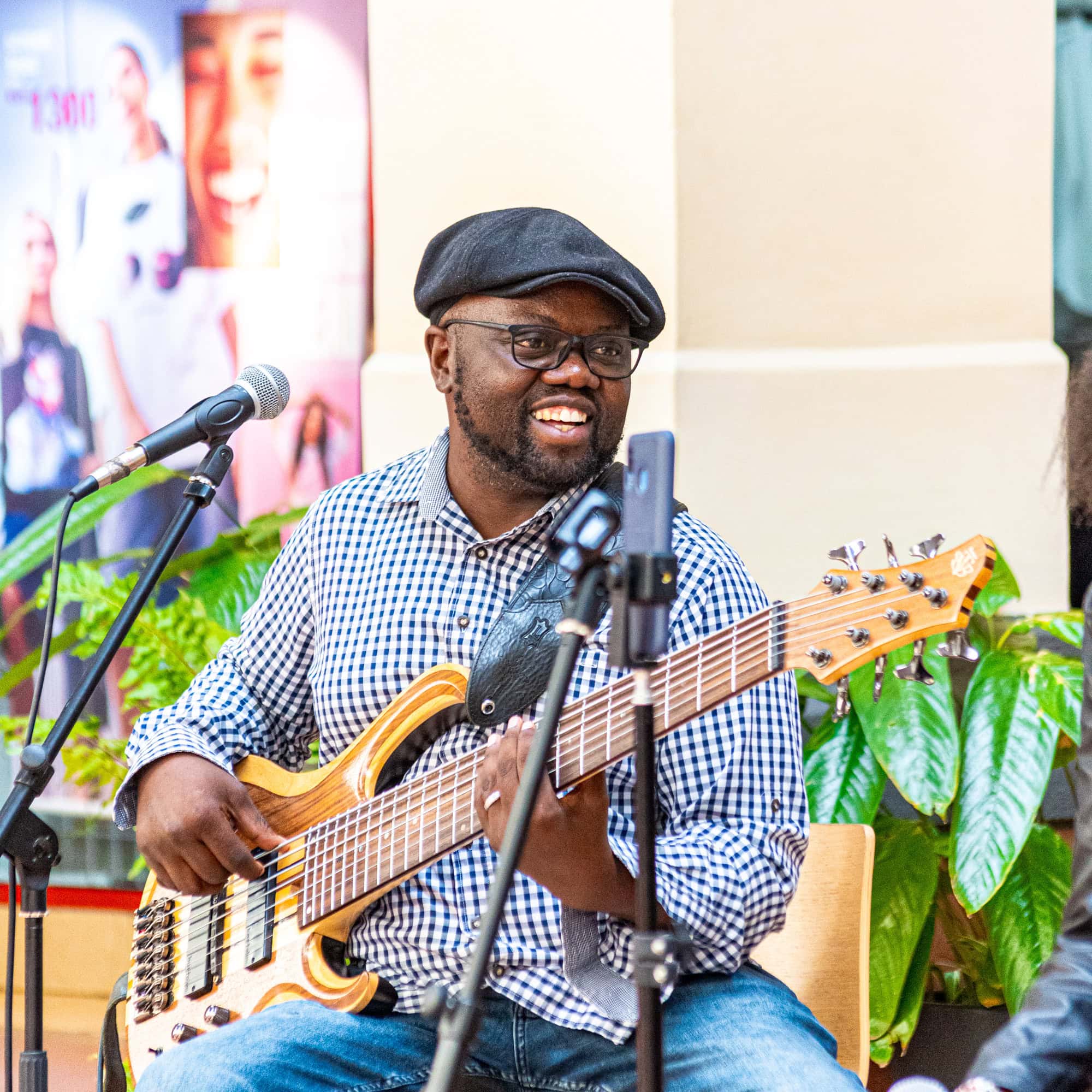 Smiling musician in a flat cap playing a bass guitar beside a microphone