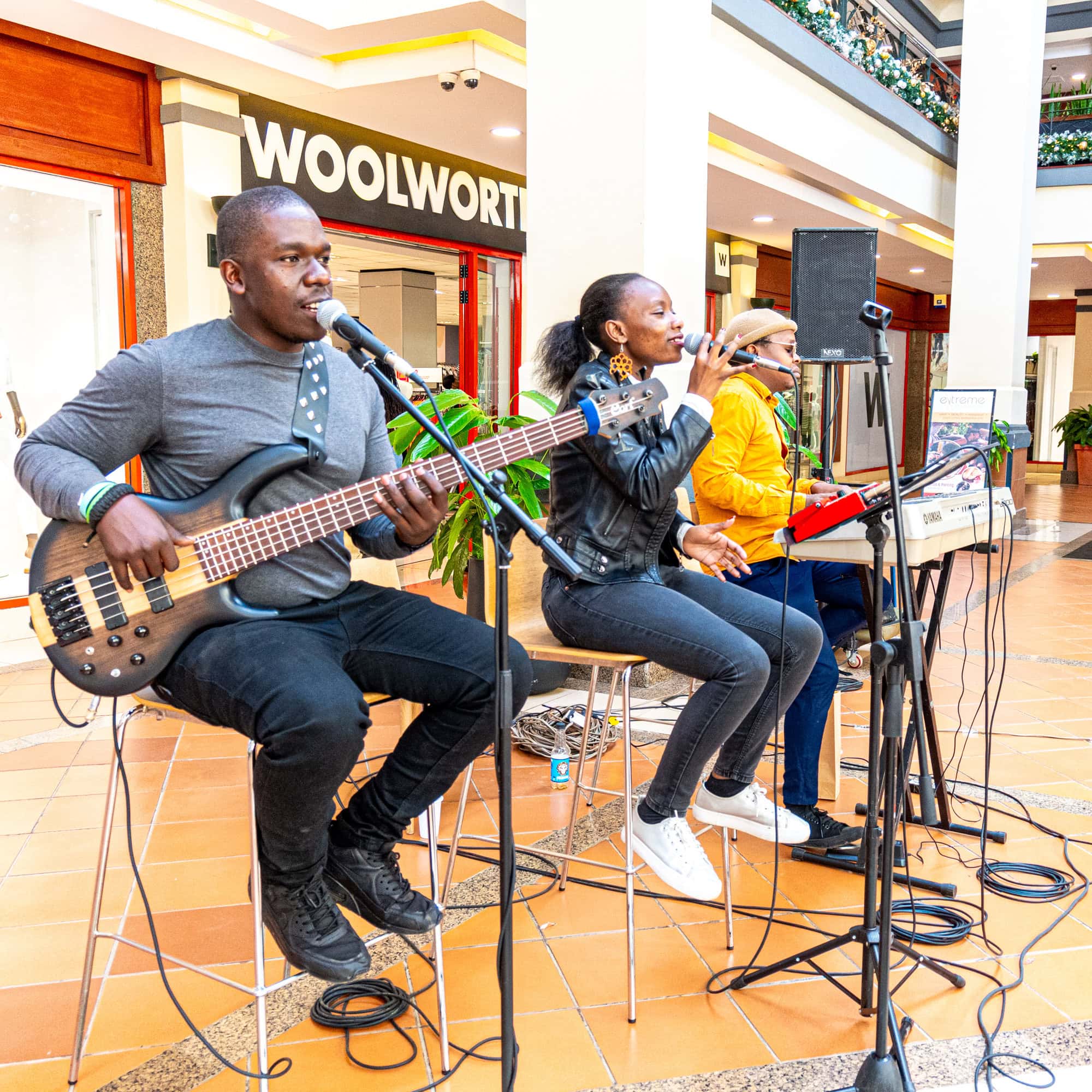 Musicians performing with bass guitar, microphones, and audio equipment in a shopping mall