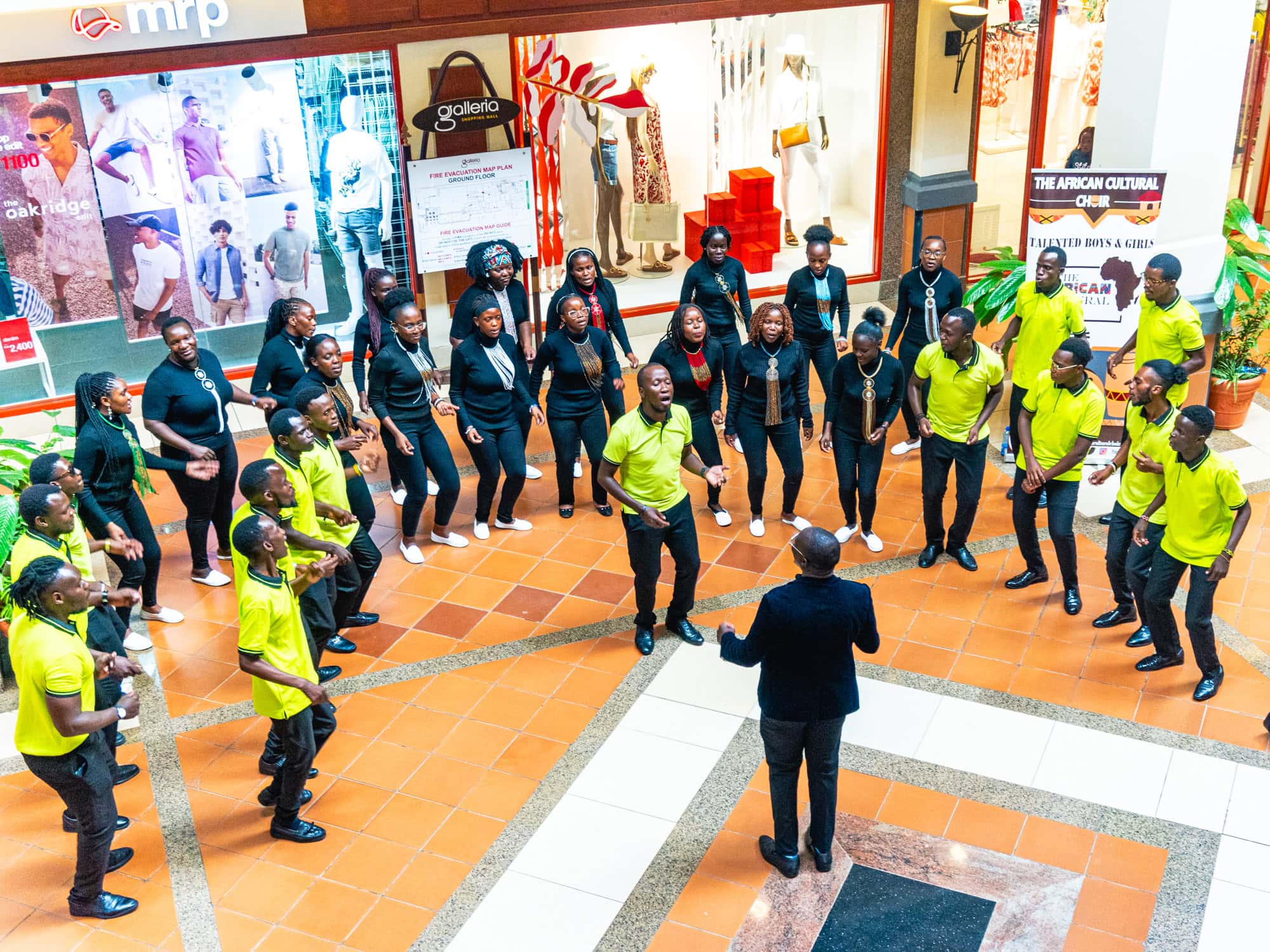 Large group of performers in lime green and black shirts gather in a shopping mall atrium