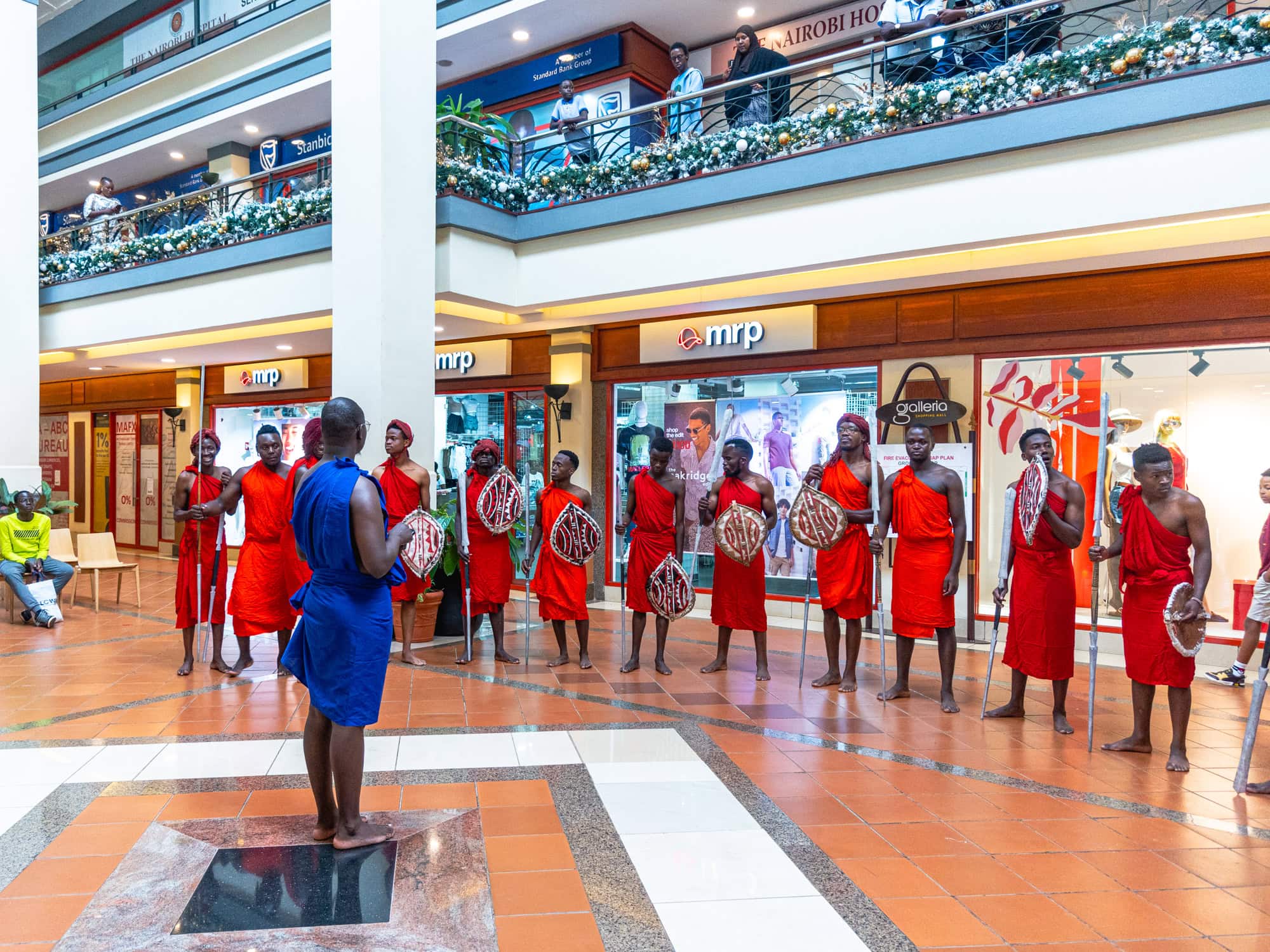 Cultural performers in red clothing stand in a line holding decorated shields
