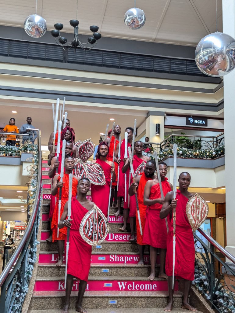 Group of performers in red clothing holding staffs and decorative shields on a mall staircase