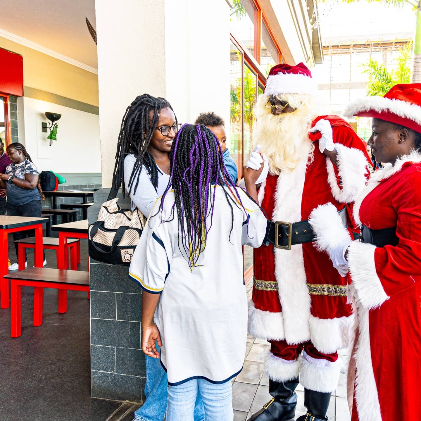 Santa Claus greeting children beside a woman dressed as Mrs. Claus in a shopping area