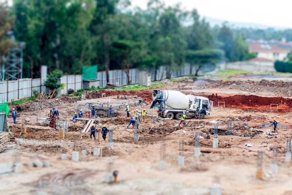 A wide view of a construction site with workers, foundation columns, and a cement mixer