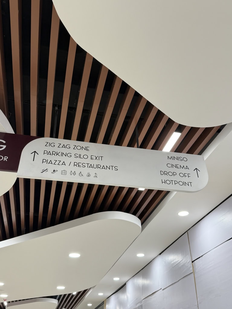 Directional sign pointing to the Zig Zag Zone, parking and restaurants, with curved white ceiling panels above