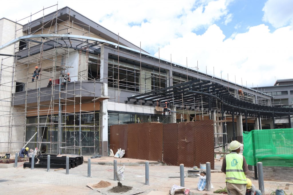 Workers construct a steel canopy on a building facade surrounded by scaffolding