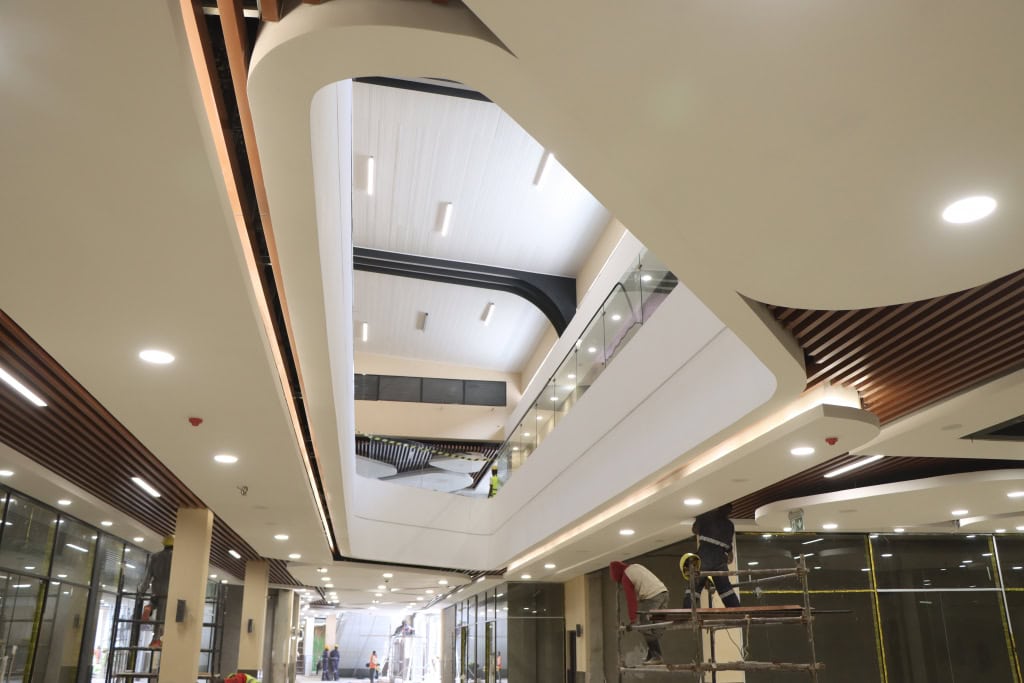 Workers carry out finishing work in a mall corridor with a large atrium and curved ceiling.