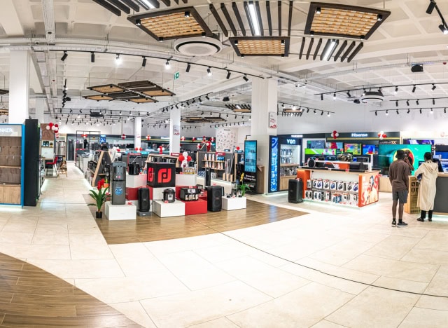 Wide view of a bright appliance showroom with product displays, branded sections, and shoppers