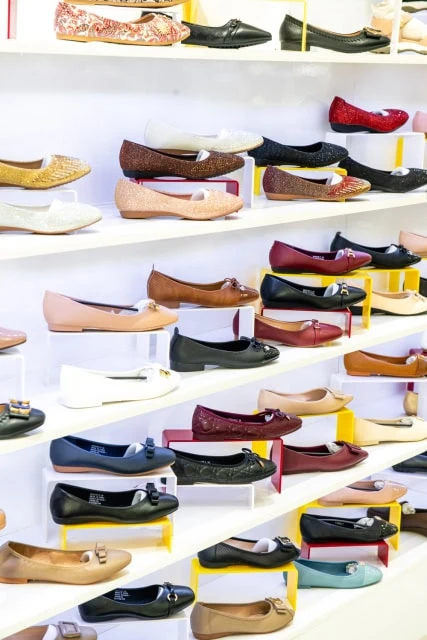 Rows of women's flats and low-heeled shoes in assorted colors displayed on white shelves.
