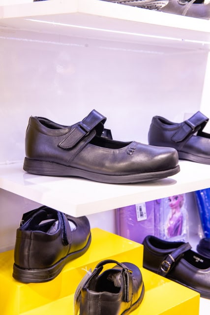 Black children's shoes displayed on white and yellow shelves