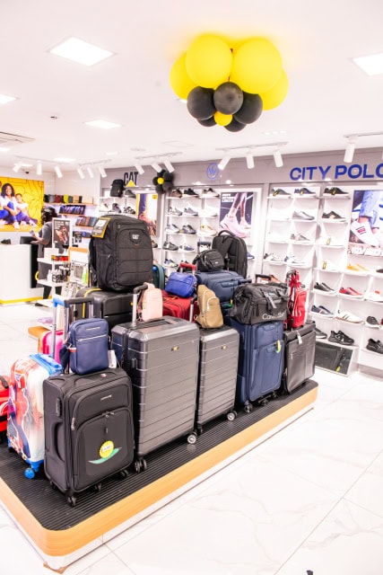 Bright store interior with rows of luggage, shoes, and black-and-yellow balloons