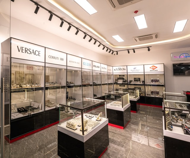 A spacious watch and jewellery showroom with glass display cases, central counters, and multiple brand signs.