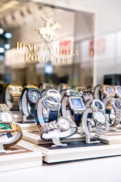 A display of watches in various colours and styles behind glass with Beverly Hills Polo Club branding.