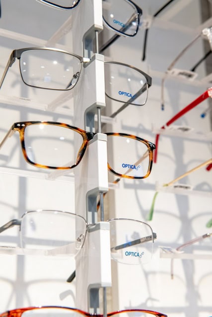 Rectangular eyeglass frames displayed on a central rack with Optica branding