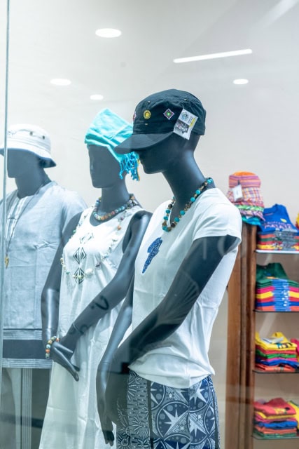 Mannequins displaying white tops, patterned trousers, caps, and beaded necklaces
