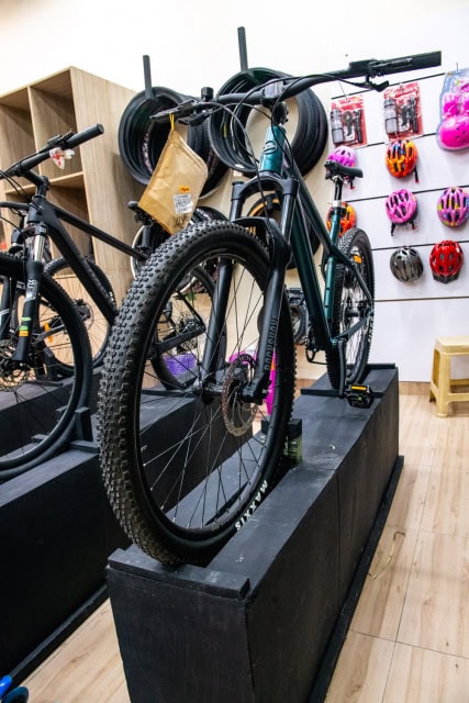 Bicycles displayed on black platforms inside a store with helmets and accessories on the wall behind.