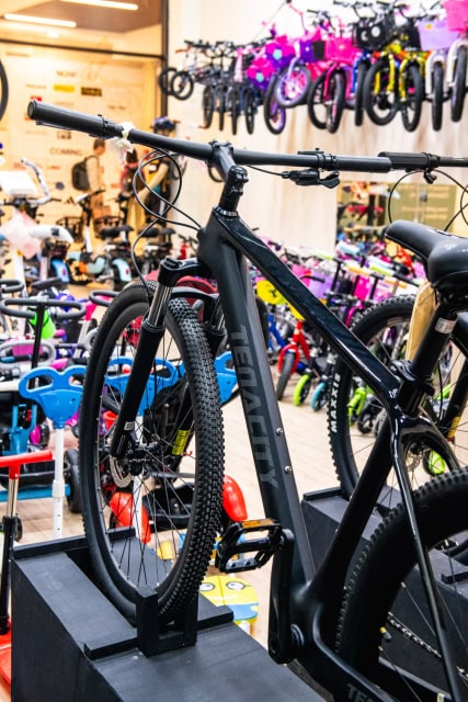 A black mountain bike displayed on a stand with other bicycles visible behind it