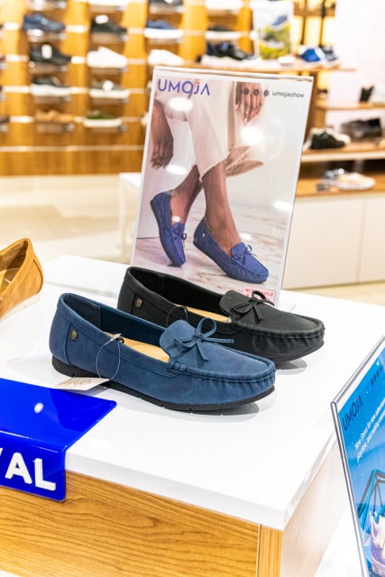 Blue and black loafers displayed on a white store counter beneath a footwear promotional card
