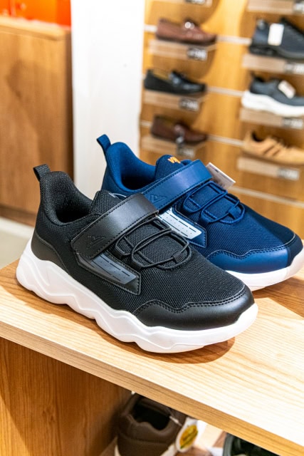 Black and blue athletic sneakers displayed on a wooden retail shelf.