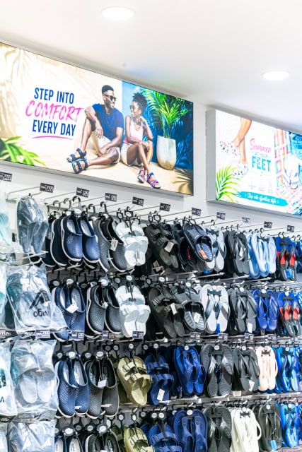 A retail wall filled with sandals and flip-flops beneath colorful promotional banners.