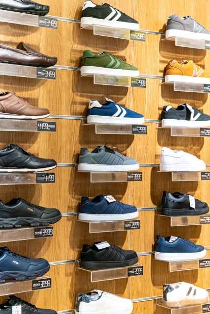 Close-up of assorted men’s and casual shoes displayed on clear shelves against a wood-paneled wall.