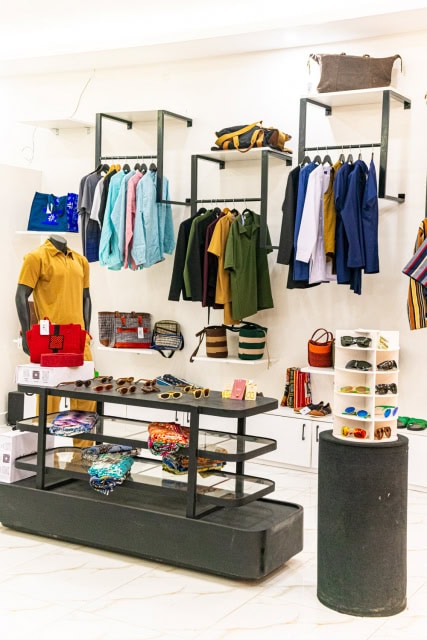 Bright store interior showing clothing racks, accessories, bags, folded textiles, and display tables.