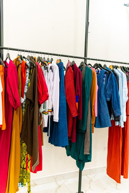 A clothing rail filled with colorful shirts, dresses, jackets, and trousers.