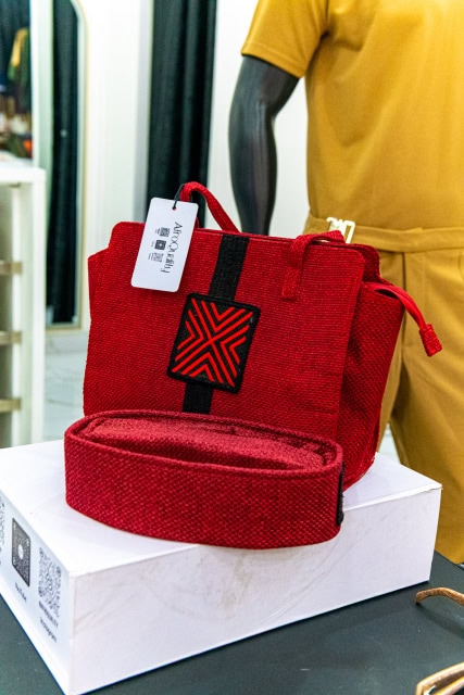 Red woven handbag with a matching pouch displayed on a white box beside a mannequin