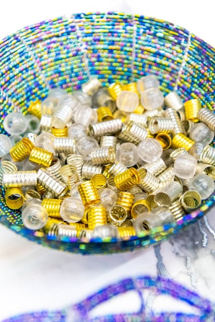 Multicolored beaded bowl filled with small gold, silver, and translucent craft components
