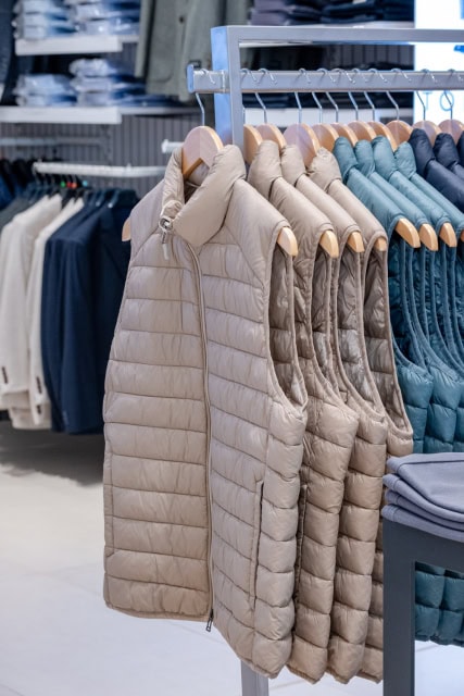 Quilted beige, cream and blue sleeveless jackets hanging on a retail rack