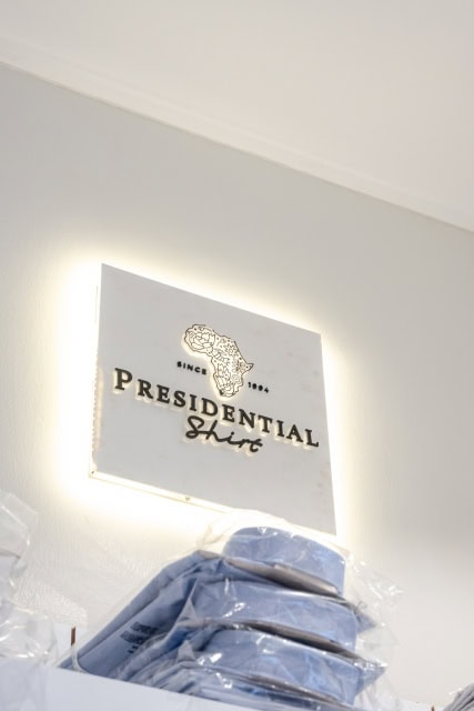 Illuminated Presidential Suite sign mounted above packaged blue shirts