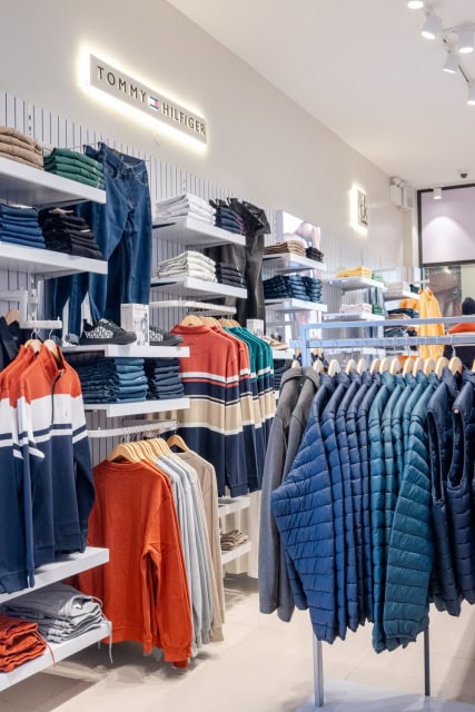 Wide view of a fashion store interior with folded clothes, hanging jackets and illuminated brand signage