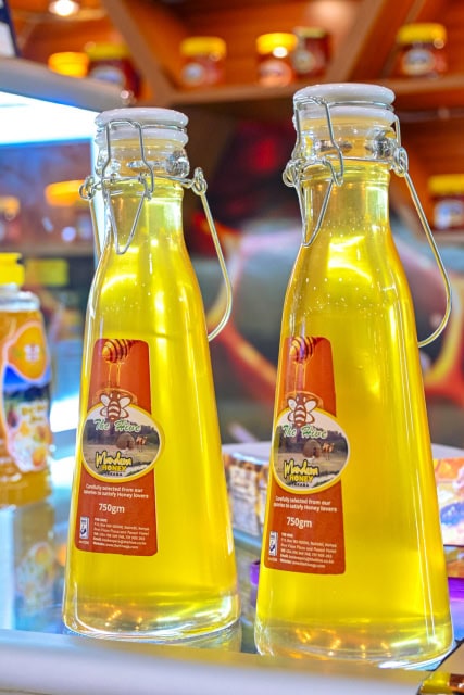 Two tall glass bottles of golden honey displayed on a retail shelf