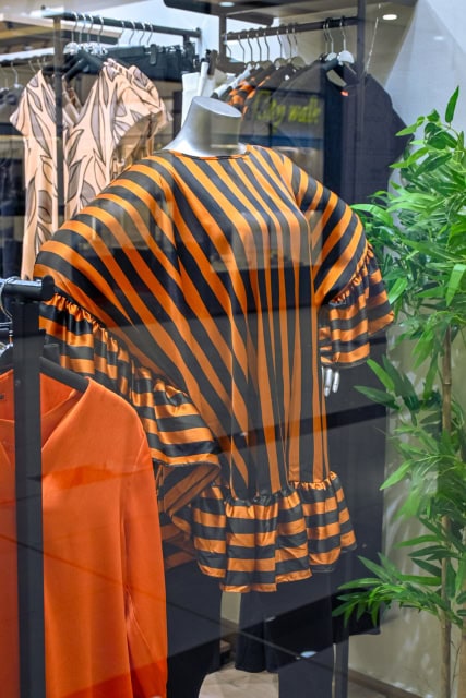 A mannequin wearing an orange and black striped top in a clothing store window