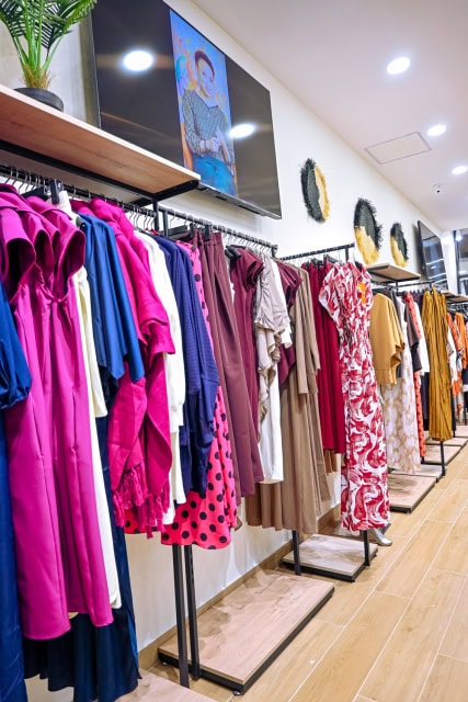 Clothing store aisle with colorful garments on racks, wall decorations and overhead screens