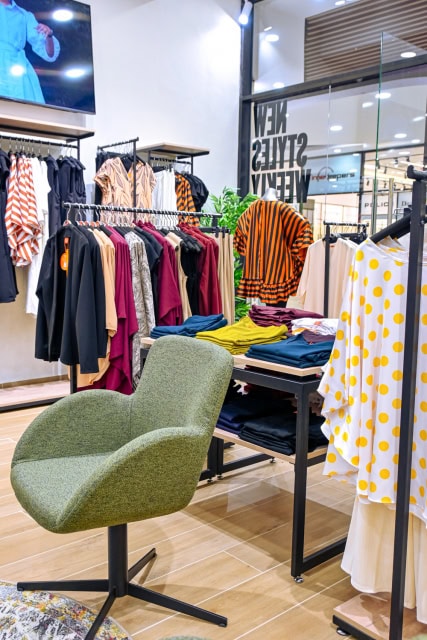 Fashion store interior with clothing racks, folded garments, a green chair and plants