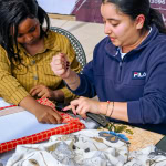 A participant and facilitator stretch patterned fabric around a frame during the Frame and Fabric Workshop.