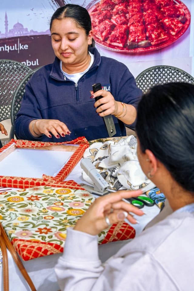A facilitator demonstrates a crafting tool while a participant follows along at the Frame and Fabric Workshop.