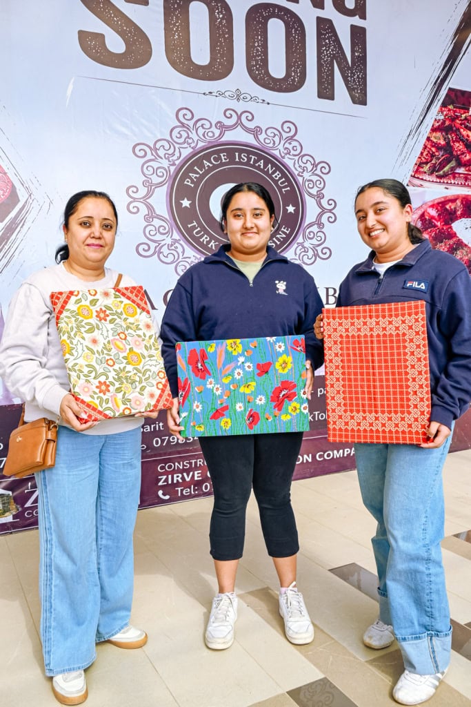 Three smiling participants display colourful finished fabric panels at the Frame and Fabric Workshop.