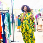 Connie Oluoch speaks into a microphone while standing among clothing racks at Style, Shop & Sip.