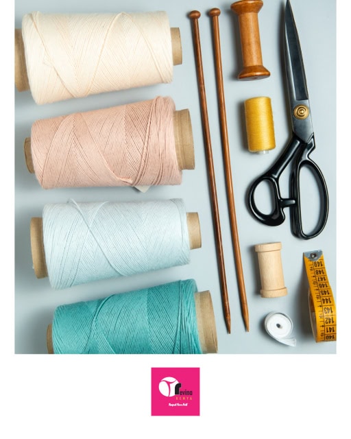 Sewing supplies arranged on a pale surface, including thread spools, wooden tools, scissors, a measuring tape, and small notions.