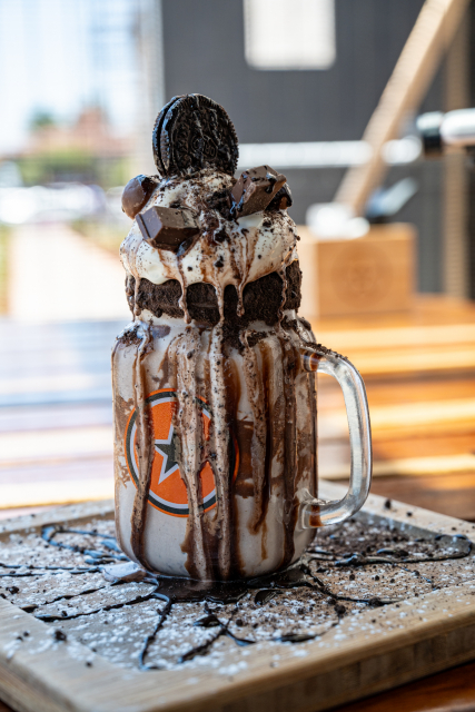 Tall chocolate milkshake in a handled glass mug topped with whipped cream, cookie crumbs and chocolate pieces.