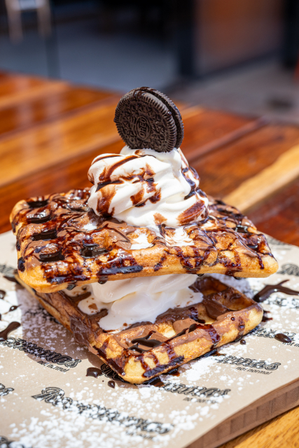 Chocolate-drizzled waffle sandwich topped with whipped cream and a chocolate sandwich cookie.