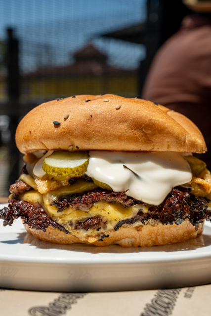 Stacked cheeseburger with a sesame bun, melted cheese, pickles and creamy sauce.