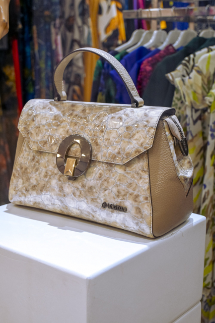 Beige textured handbag with a metal clasp displayed on a white pedestal.