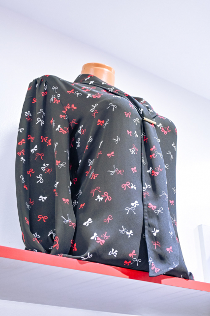 Black long-sleeved garment with red, pink, and white bow motifs displayed on a mannequin